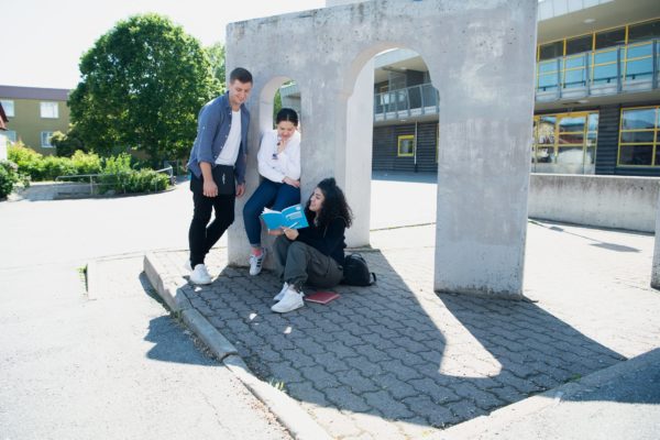 Några personer hänger ute vid en staty och pluggar