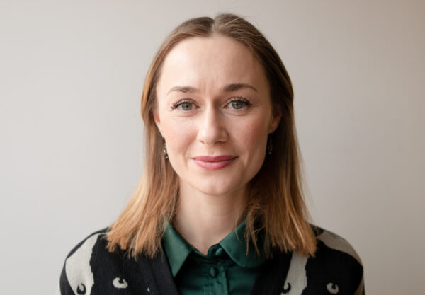 Porträttbild av person som står mot en vit bakgrund och tittar in i kameran och ler