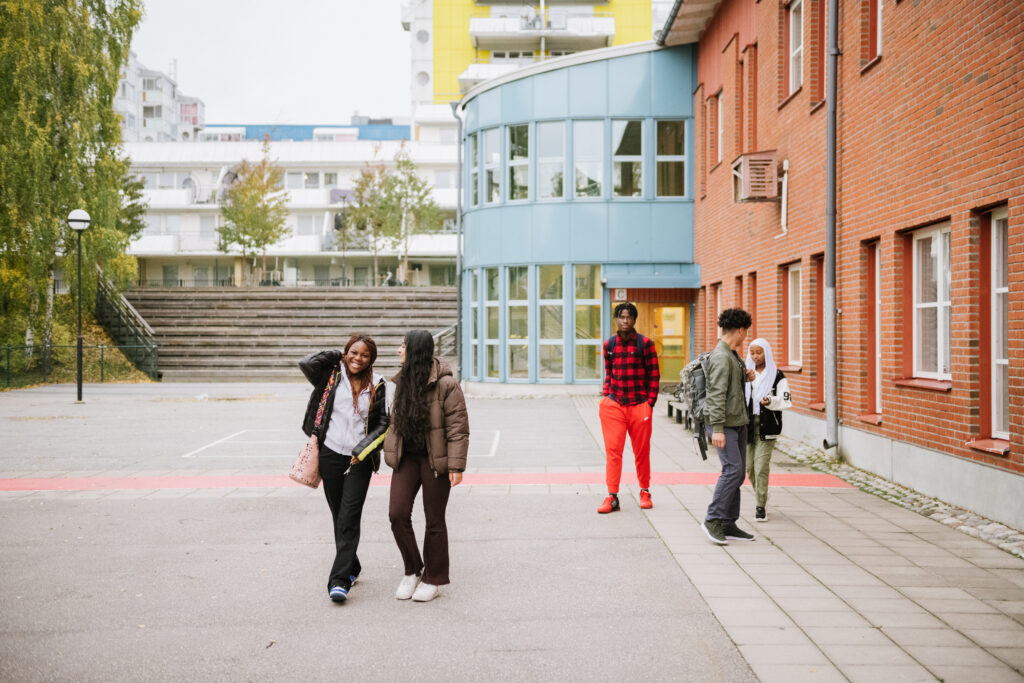 Fem elever lämnar skolbyggnaden och går mot kameran ute på en skolgård