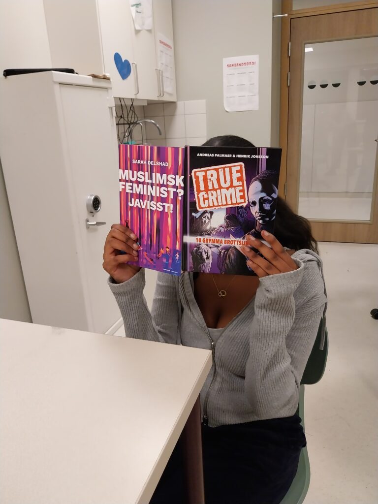 En elev sitter i ett klassrum och håller upp en bok framför ansiktet. På boken står det "True crime".