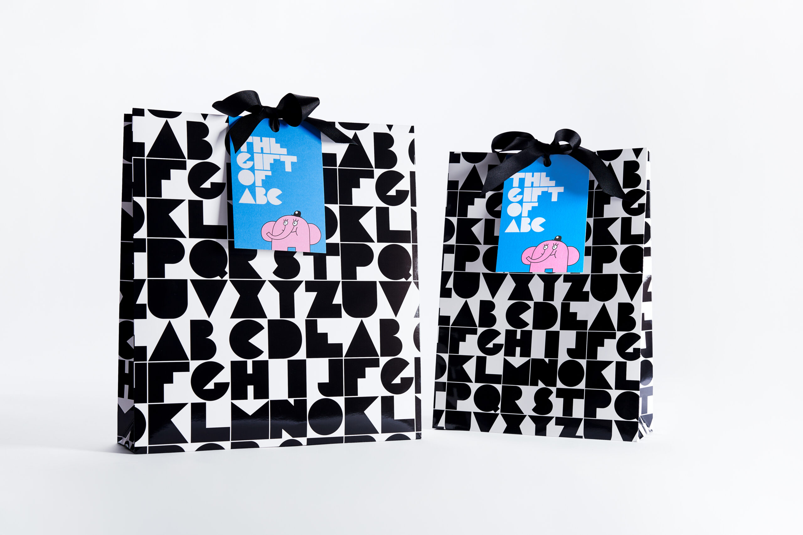 Två presentpåsar i svartvitt tryck. På påsarna sitter ett blått kort knuten med en svart rosett. På det blåa kortet syns texten "The Gift of ABC" och Owe Gustafsons illustration av en rosa elefant från "Fem myror är fler än fyra elefanter."