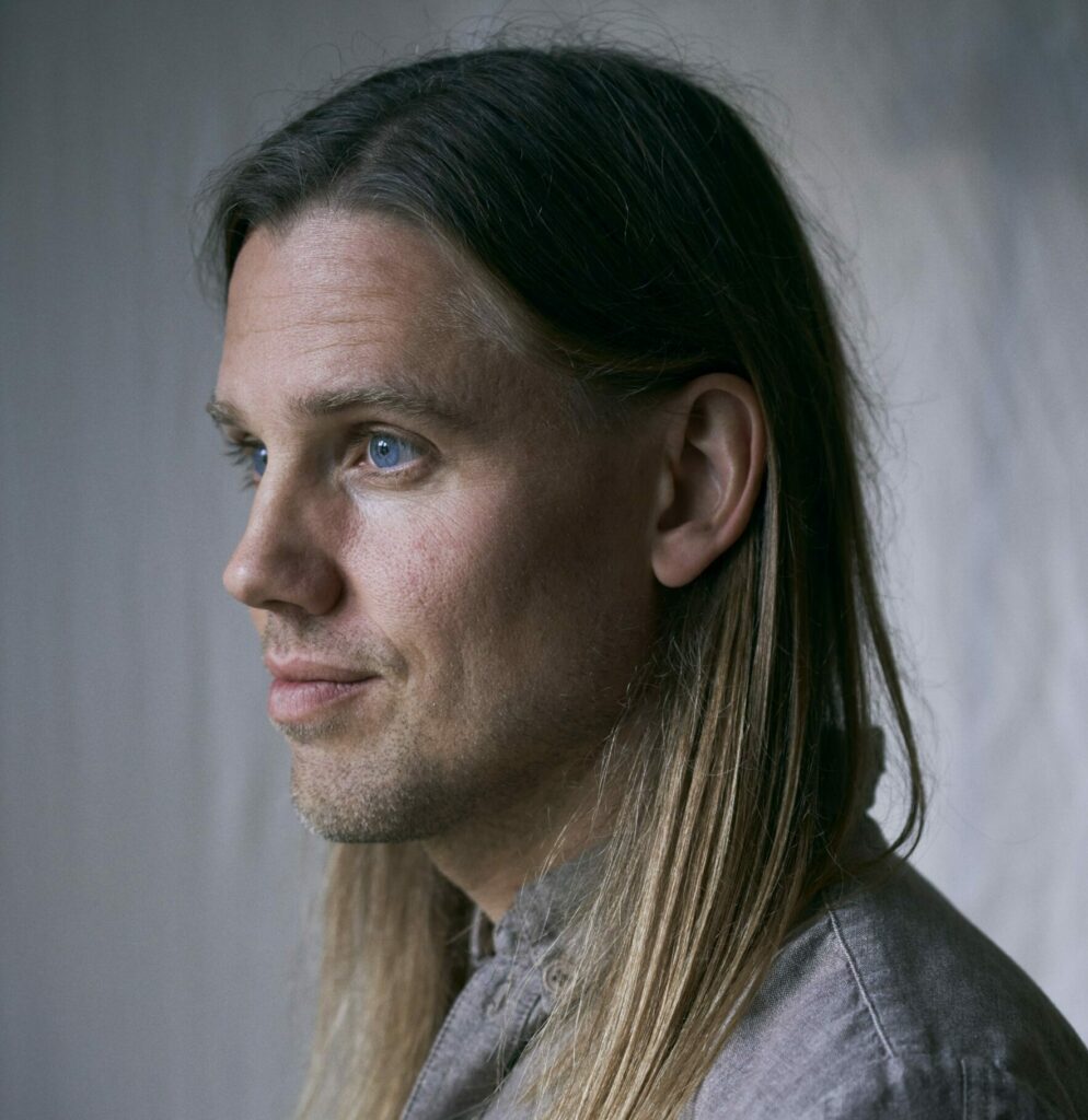 Bild av en man i skjorta med axellångt hår. Bilden är tagen i profil och i gråa toner.
